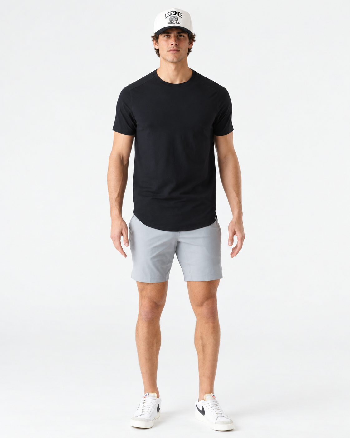 Black short-sleeve t-shirt with curved hem, worn with gray shorts and white sneakers.