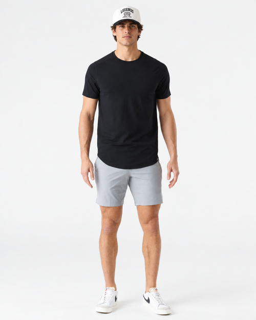 Black short-sleeve t-shirt with curved hem, worn with gray shorts and white sneakers.