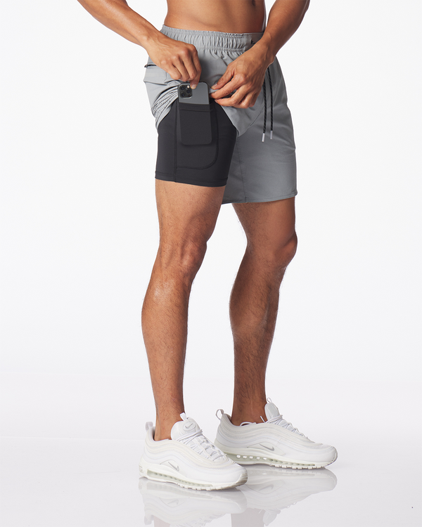 Men's medium gray shorts with black inner shorts and side pocket, worn with white sneakers.