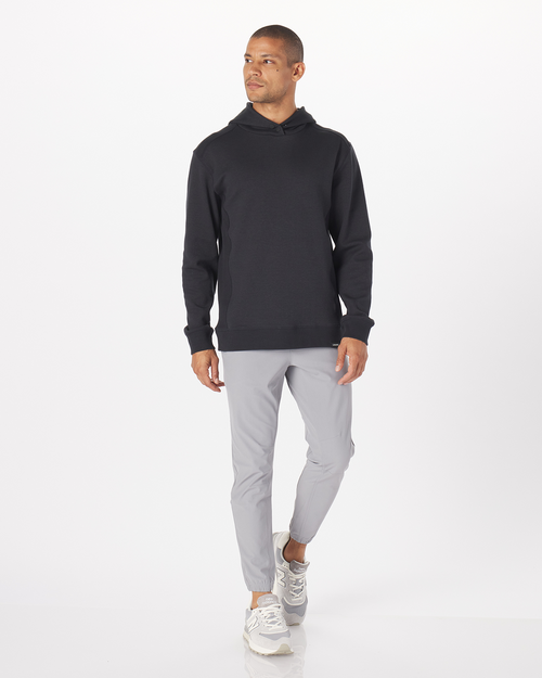 Black pullover hoodie with drawstring hood and ribbed cuffs, shown on model with gray pants.