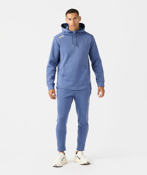 Man wearing heather blue Hawthorne Tech Jogger set with hoodie, kangaroo pocket, and tapered jogger pants.