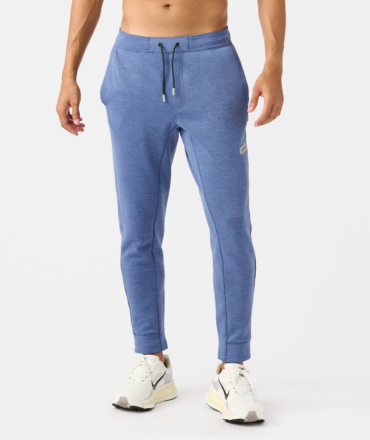 Man wearing heather blue joggers with drawstring waist and white sneakers.