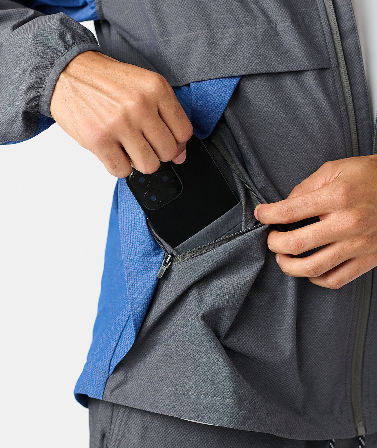 Charcoal full-zip jacket with blue interior lining, worn with hand holding open pocket containing a smartphone.