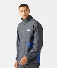 Man wearing charcoal and blue full-zip hooded jacket with white brand label on chest.