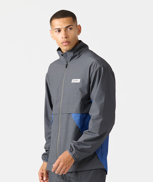 Man wearing charcoal and blue full-zip hooded jacket with white brand label on chest.