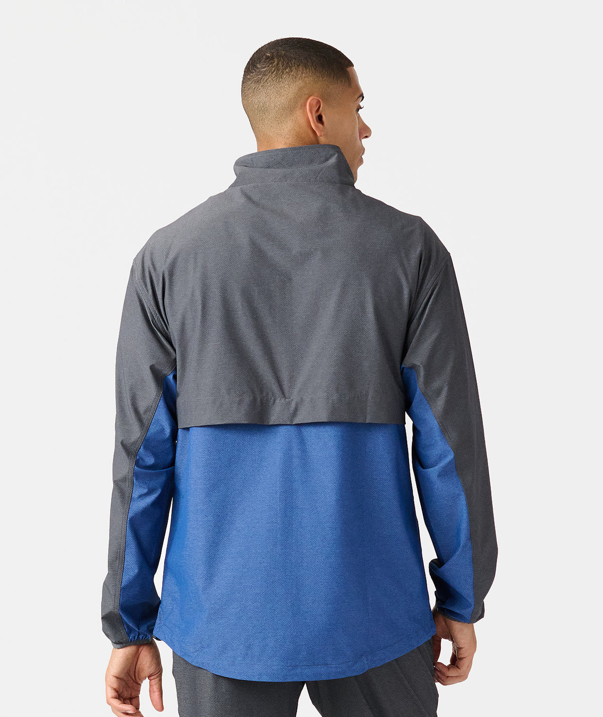 Man wearing charcoal and blue colorblock full-zip jacket with high collar, shown from back.