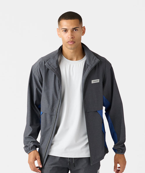 Charcoal full-zip jacket with blue side panels and branded chest patch worn over white t-shirt.