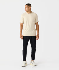Man wearing black tapered pants with cream t-shirt and white sneakers.
