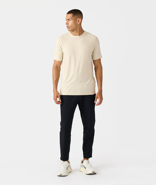 Man wearing black tapered pants with cream t-shirt and white sneakers.