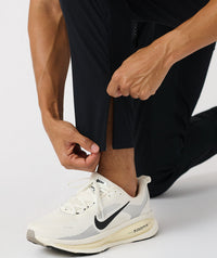 Black tapered pants with side seam detail shown on model wearing white sneakers.