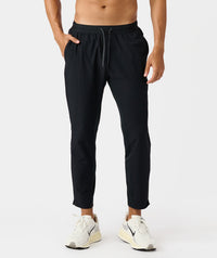 Black drawstring pants with elastic waistband and side pockets, shown on male model wearing white sneakers.