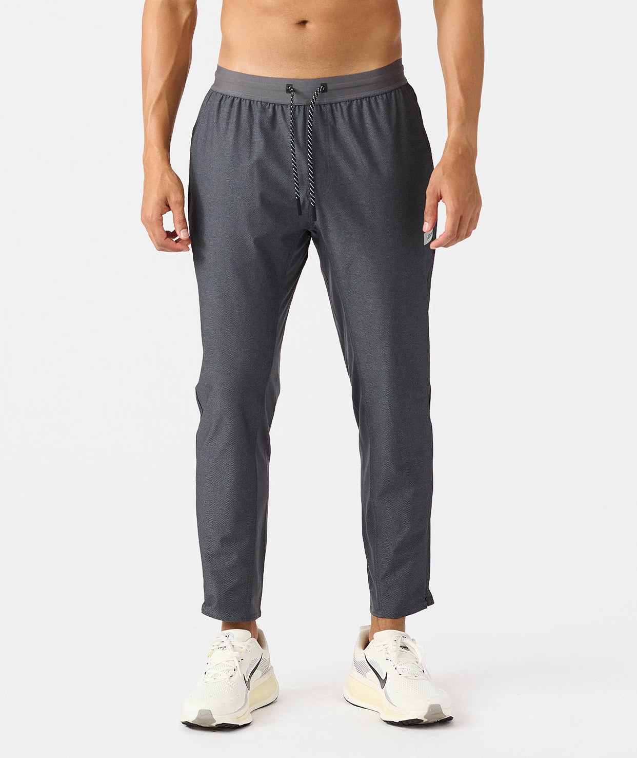 Charcoal gray joggers with elastic waistband and drawstring, tapered ankles, worn with white sneakers.