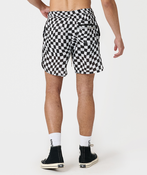 Black and white warped checkerboard mesh shorts with side pockets, shown on male model from waist down.