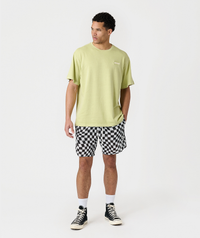 Man wearing lime green t-shirt and black-and-white checkerboard mesh shorts with white socks and black canvas sneakers.