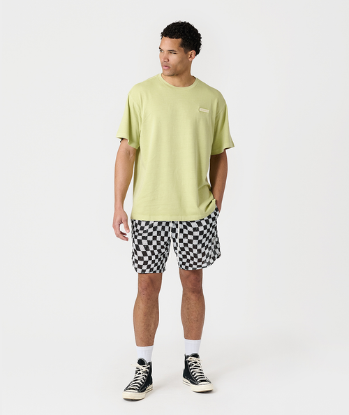 Man wearing lime green t-shirt and black-and-white checkerboard mesh shorts with white socks and black canvas sneakers.