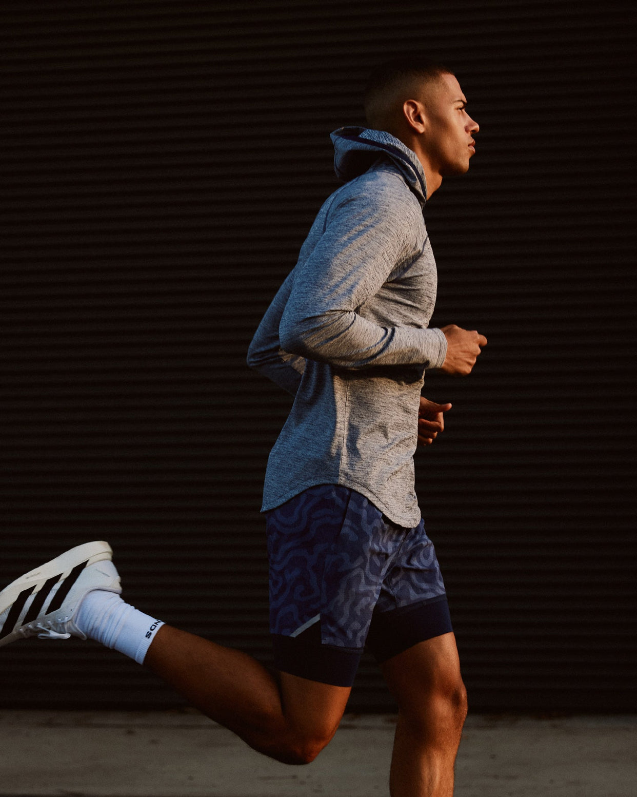 Man jogging wearing ocean heather hooded long-sleeve shirt with blue hood and patterned shorts.