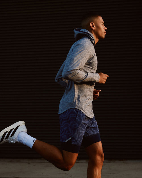 Man jogging wearing ocean heather hooded long-sleeve shirt with blue hood and patterned shorts.