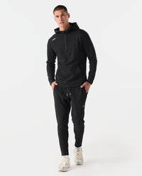 Man wearing black heather half-zip hoodie and matching joggers with drawstring waist and cuffed ankles.