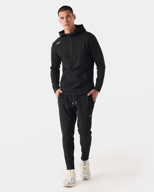 Man wearing black heather half-zip hoodie and matching joggers with drawstring waist and cuffed ankles.