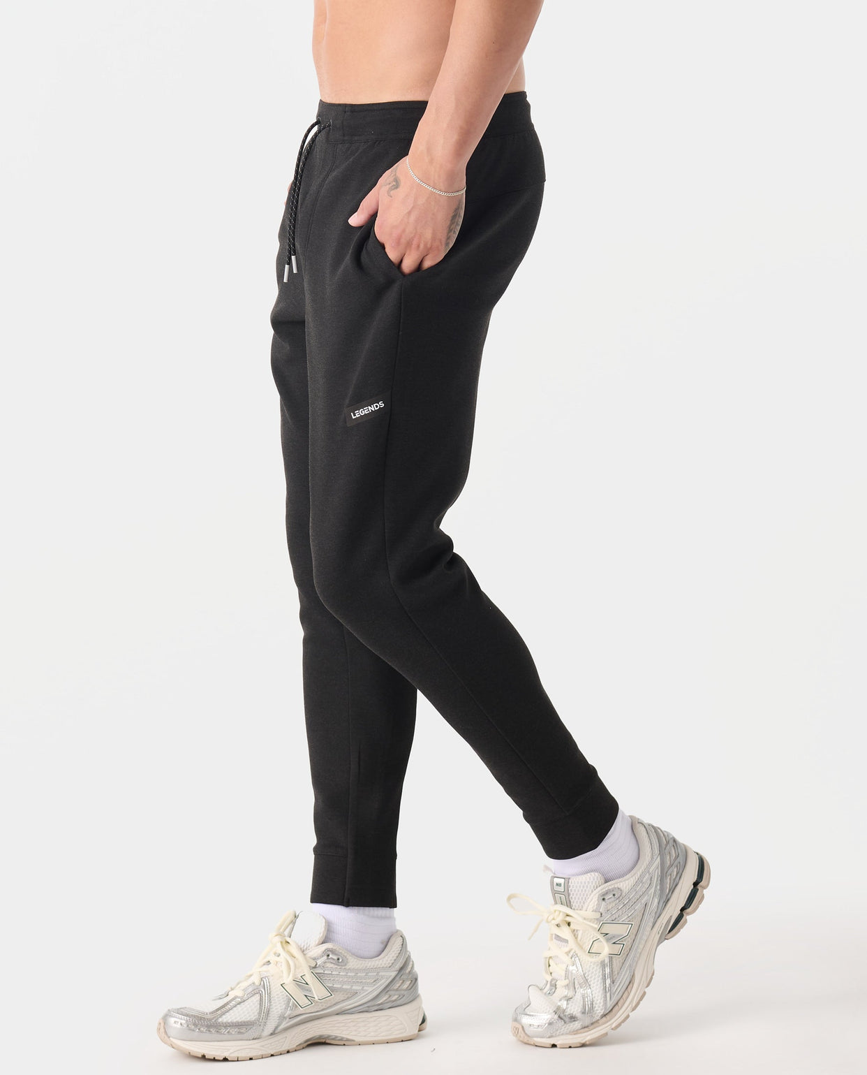 Black heather joggers with drawstring waist and side pockets, worn with white socks and beige sneakers.