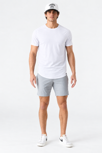White short-sleeve t-shirt with curved hem on male model wearing gray shorts and white sneakers.