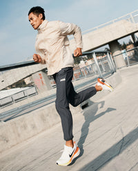 Man jogging outdoors wearing charcoal gray joggers with a cream jacket and white sneakers with orange accents.