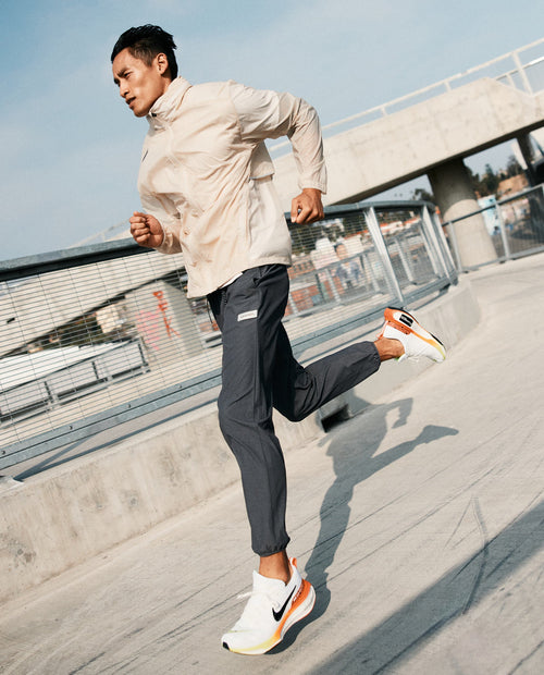 Man jogging outdoors wearing charcoal gray joggers with a cream jacket and white sneakers with orange accents.