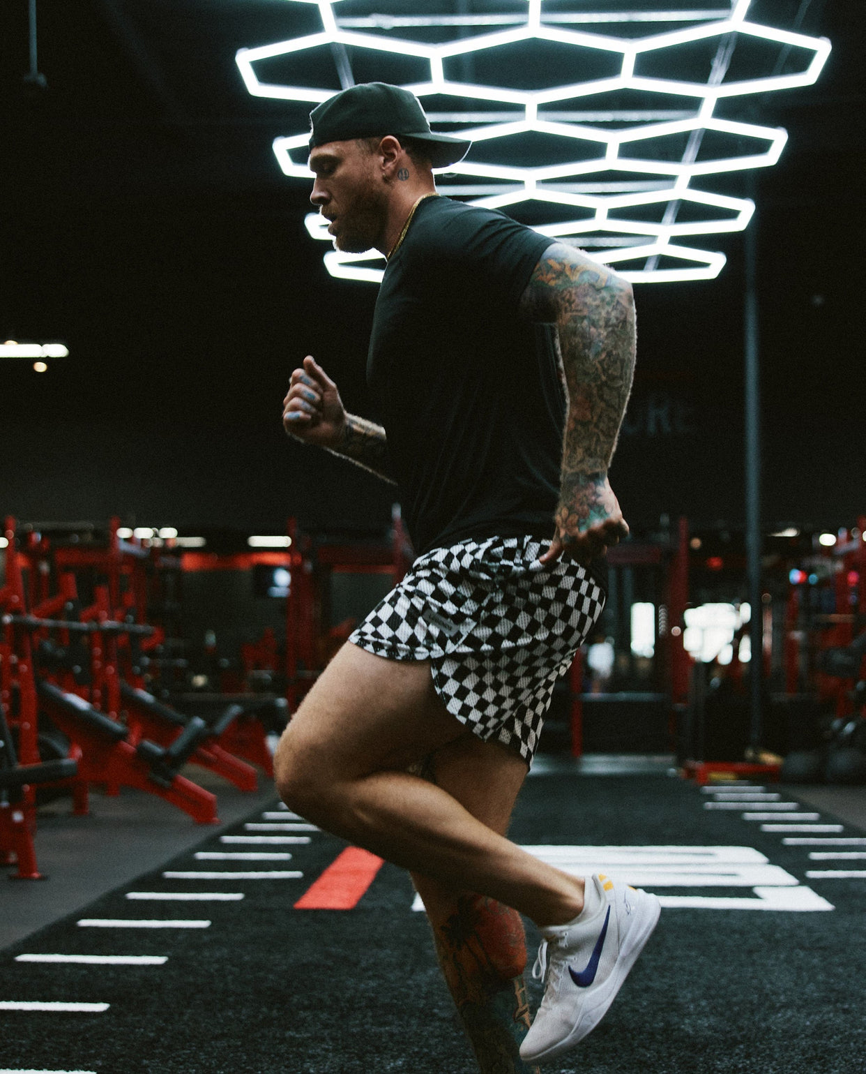 Man wearing black and white warped checkerboard mesh shorts while running in a gym.