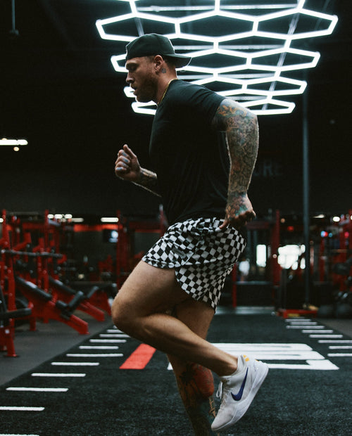 Man wearing black and white warped checkerboard mesh shorts while running in a gym.