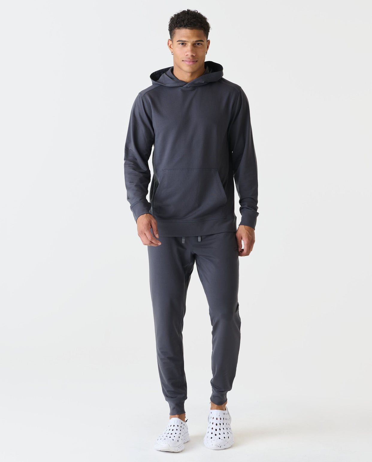 Charcoal gray hoodie with kangaroo pocket and matching joggers worn by model with white sneakers.